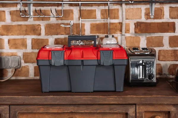 Close-up shot of toolbox standing on kitchen table with toaster in front of brick wall — Stock Photo