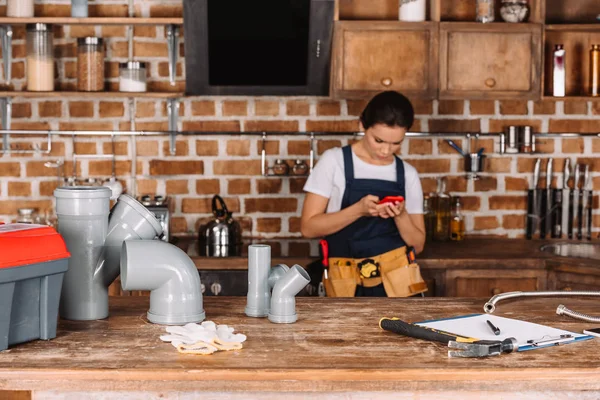 Bellissimo giovane idraulico femminile utilizzando smartphone in cucina — Foto stock