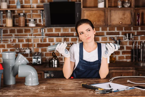 Thoughtful young female plumber with plastic pipes at kitchen — Stock Photo