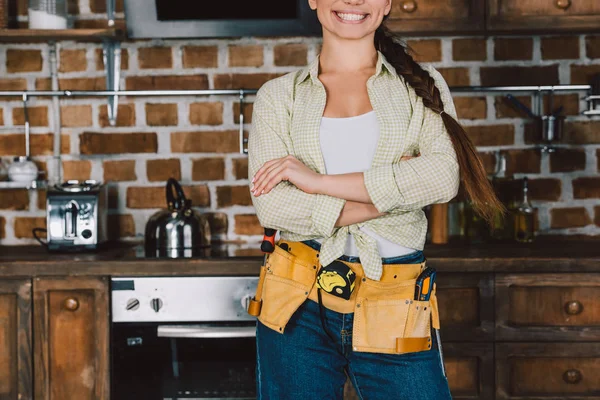 Abgeschnittene Aufnahme einer lächelnden Reparaturfrau mit verschränkten Armen, die vor einem Küchentisch mit Backofen steht — Stockfoto