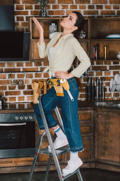 Bela jovem reparadora de pé na escada rolante na cozinha e olhando para cima — Fotografia de Stock