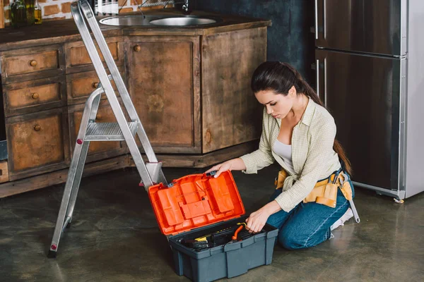 Bella giovane riparatrice con cassetta degli attrezzi seduta sul pavimento della cucina — Foto stock