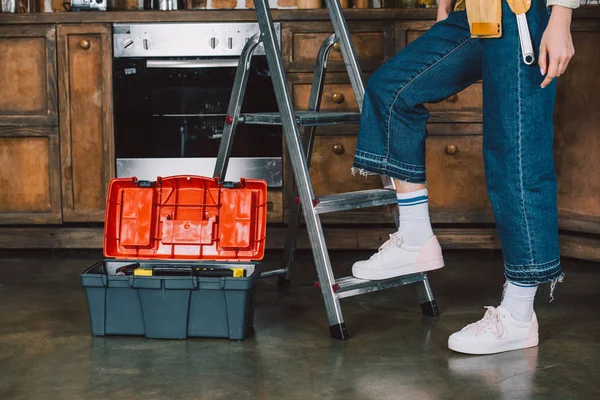 Cropped shot of repairwoman in jeans standing on stepladder at kitchen — Stock Photo