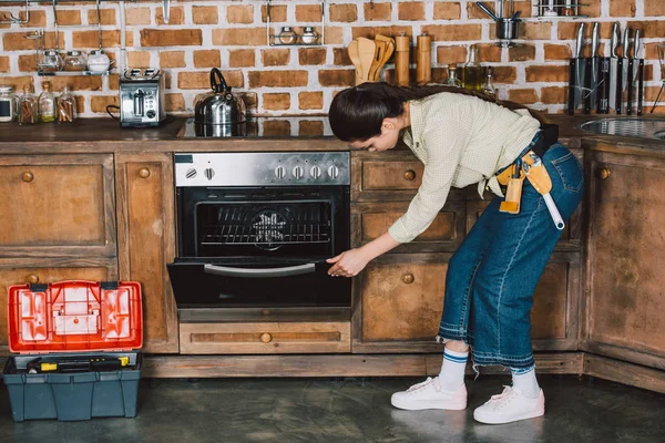 Fiduciosa giovane riparatrice esaminando forno in cucina — Foto stock
