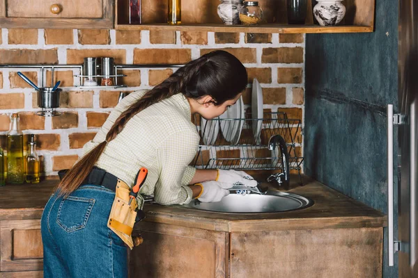 Jeune réparatrice avec clé de fixation évier de cuisine — Photo de stock