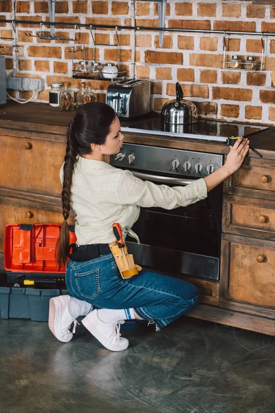 Atractiva joven reparadora que mide el ancho del horno en la cocina - foto de stock