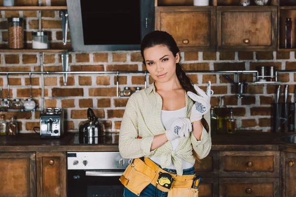 Atraente jovem reparadora em luvas de trabalho em pé na cozinha e olhando para a câmera — Fotografia de Stock