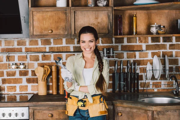 Счастливая молодая ремонтница с гаечным ключом, стоящая на кухне — стоковое фото