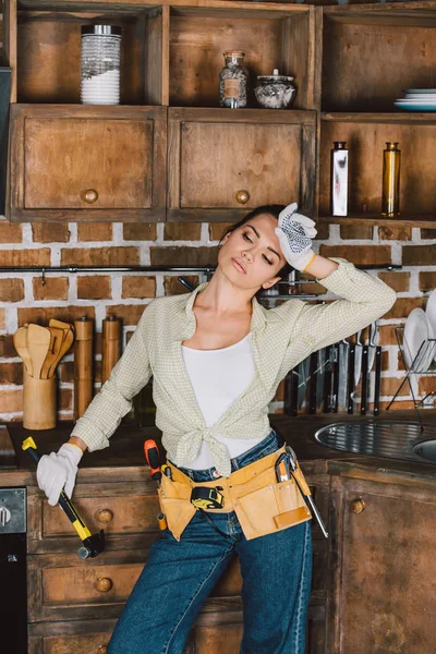 Exhausted young repairwoman with hammer wiping sweat — Stock Photo