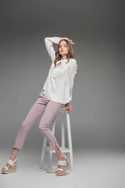 Beautiful woman sitting on chair and looking at camera on grey background — Stock Photo