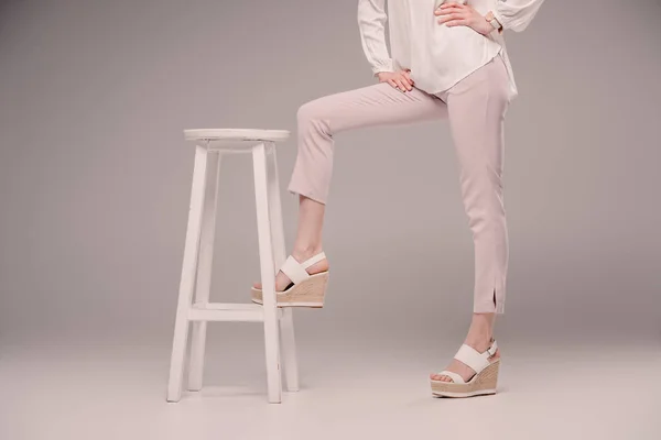 Abgeschnittenes Bild eines weiblichen Modells, das mit Bein auf Stuhl auf grauem Hintergrund steht — Stockfoto