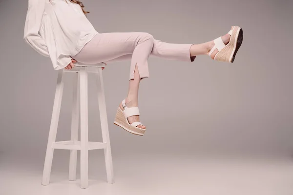 Cropped image of woman posing and showing legs on chair on grey background — Stock Photo