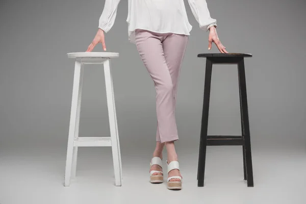 Abgeschnittenes Bild eines weiblichen Modells, das zwischen Stühlen auf grauem Hintergrund steht — Stockfoto