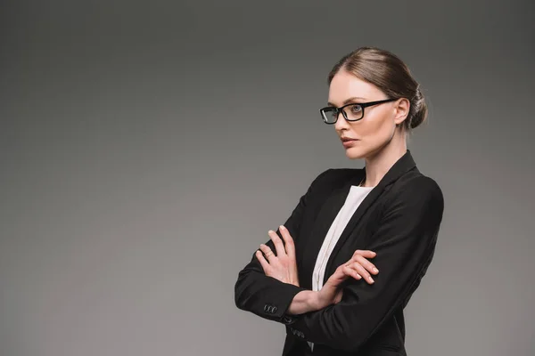 Serious businesswoman in eyeglasses standing with crossed arms isolated on grey background — Stock Photo