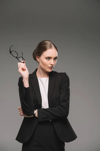 Belle femme d'affaires tenant des lunettes et regardant loin isolé sur fond gris — Photo de stock