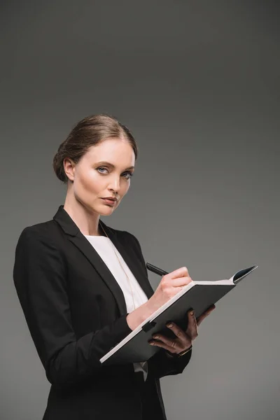 Приваблива бізнес-леді, що пише в підручнику ізольовані на сірому фоні — стокове фото