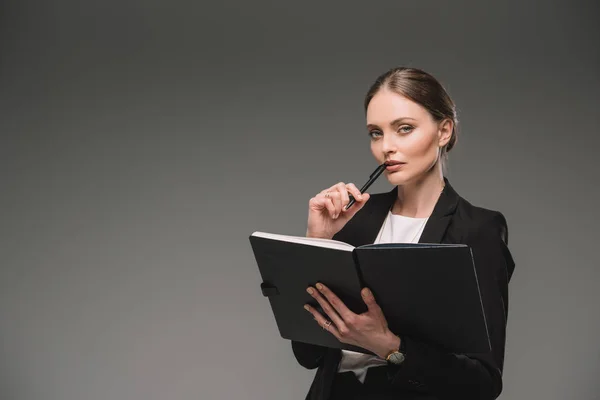 Nachdenkliche Geschäftsfrau hält Lehrbuch isoliert auf grauem Hintergrund — Stockfoto