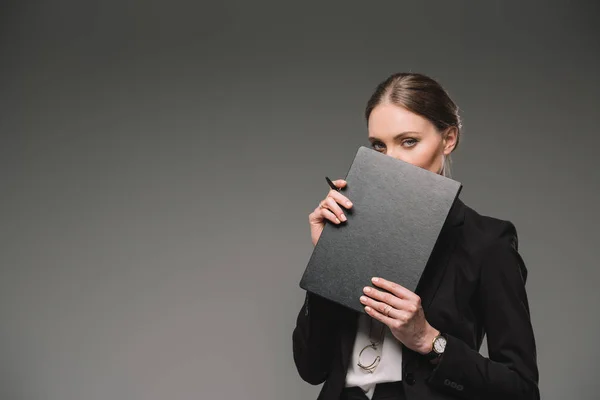Бізнес-леді, що закриває обличчя підручником ізольовано на сірому фоні — стокове фото