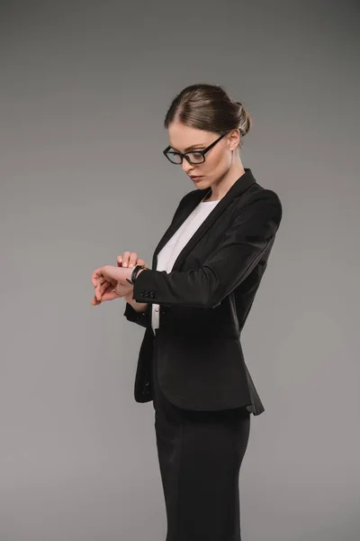 Belle femme d'affaires en lunettes regardant montre-bracelet isolé sur fond gris — Photo de stock