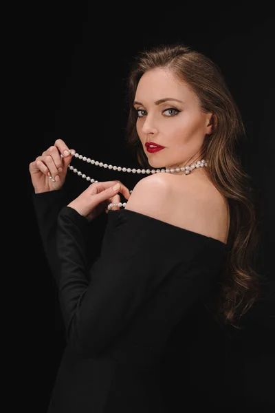 Elegant woman in black dress holding beads isolated on black background — Stock Photo