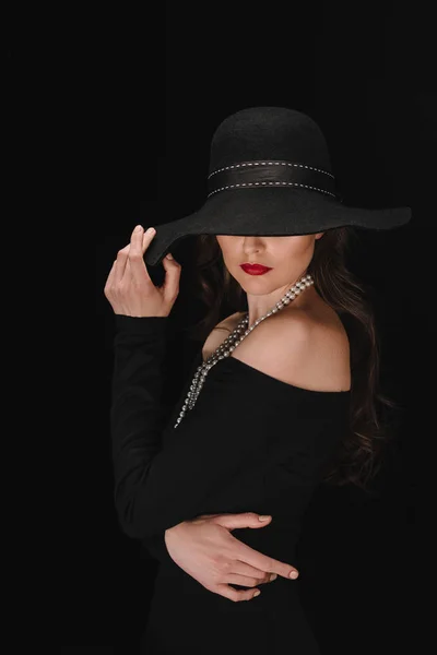 Mujer elegante en vestido negro con los ojos cubiertos por paja aislada sobre fondo negro - foto de stock