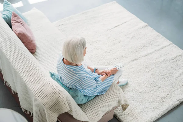 Hochwinkelaufnahme einer Seniorin mit Fernbedienung vor dem Fernseher auf dem heimischen Sofa — Stockfoto