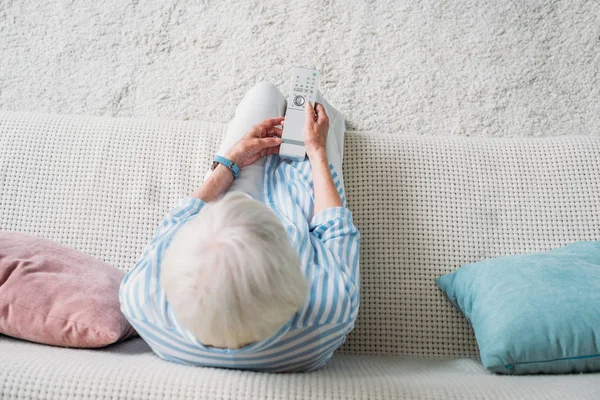 Overhead view of senior woman with remote control watching tv on sofa at home — Stock Photo