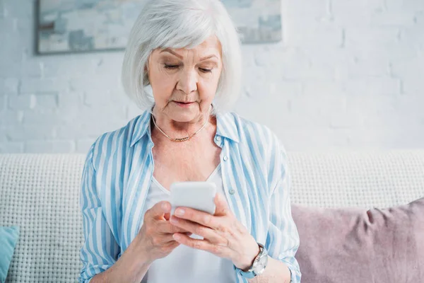 Porträt einer Seniorin, die ihr Smartphone benutzt, während sie zu Hause auf der Couch liegt — Stockfoto