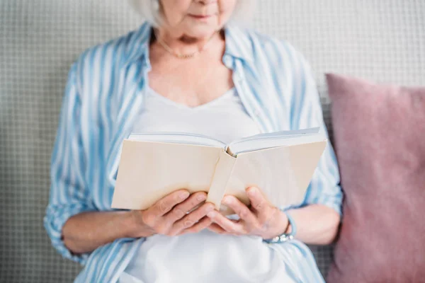 Plan recadré de livre de lecture de femme âgée tout en se reposant sur le canapé à la maison — Photo de stock