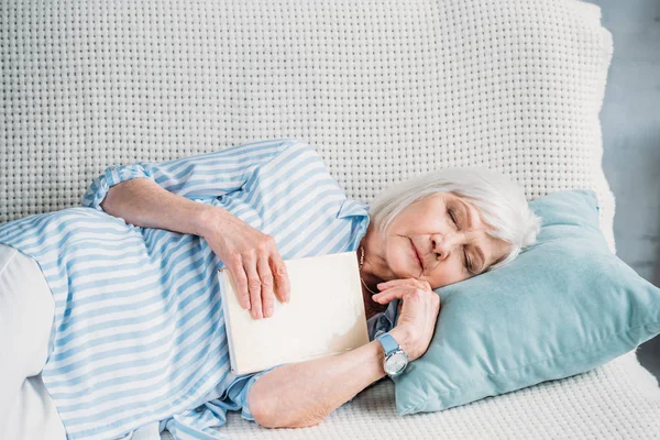 Portrait of senior woman with book sleeping on sofa at home — Stock Photo