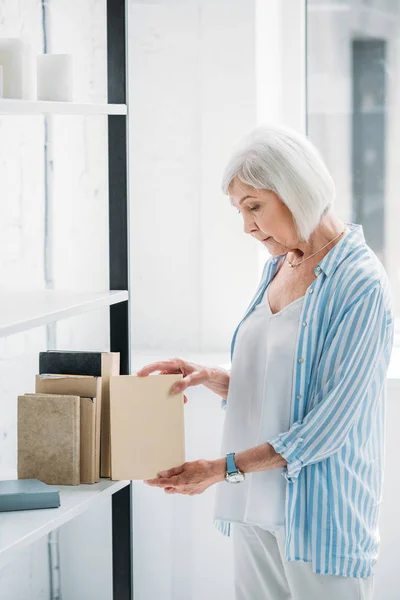 Seitenansicht einer Seniorin, die zu Hause Bücher im Bücherregal arrangiert — Stockfoto