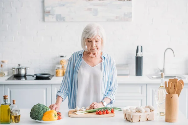 Portrait de dame âgée coupant des légumes tout en cuisinant le dîner au comptoir dans la cuisine — Photo de stock