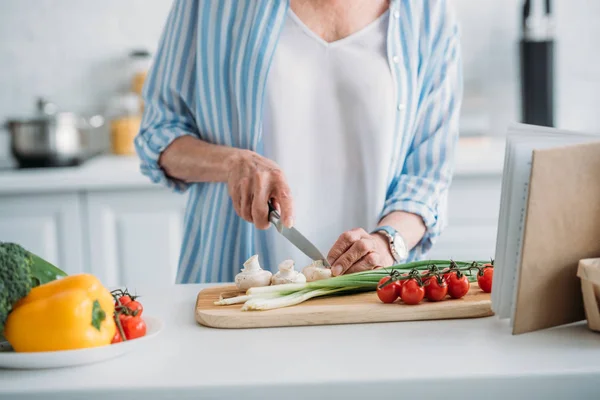 Teilansicht einer Seniorin beim Pilzschneiden beim Kochen am Tresen in der Küche — Stockfoto