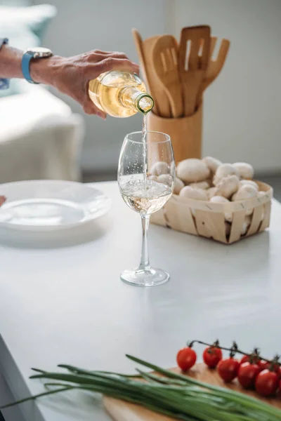 Cropped shot of senior woman pouring wine into glass at counter with fresh vegetables in kitchen — Stock Photo