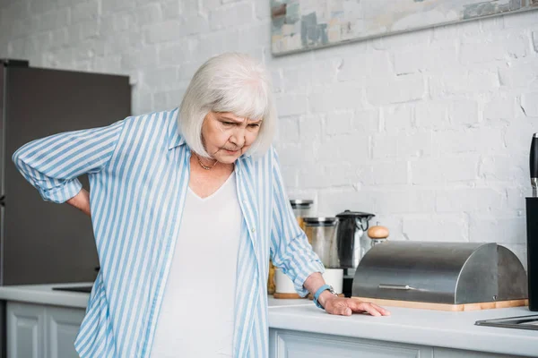 Seniorin mit Rückenschmerzen lehnt an Theke in Küche — Stockfoto