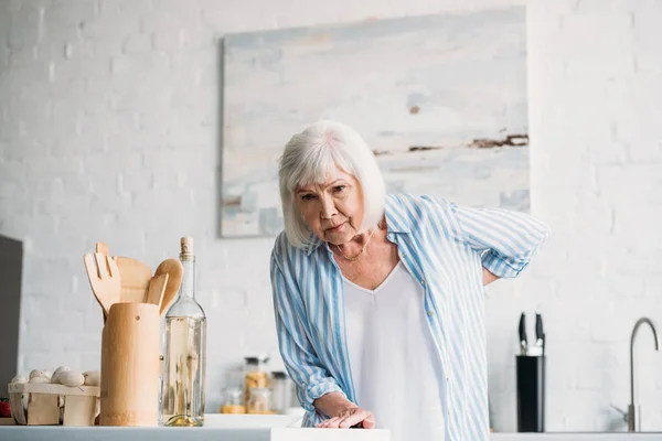 Retrato de señora mayor con dolor de espalda apoyado en el mostrador en la cocina — Stock Photo