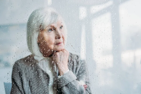 Enfoque selectivo de la mujer mayor reflexivo en chaqueta de punto mirando hacia otro lado en casa - foto de stock