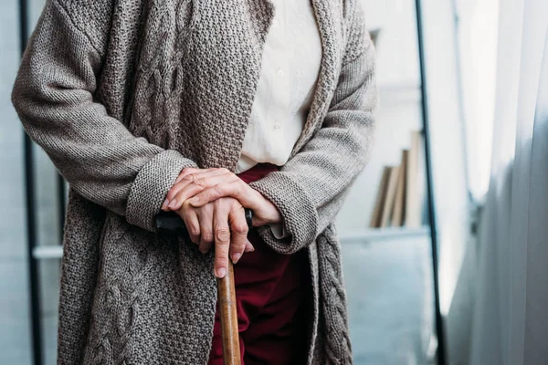 Cropped shot of senior lady with wooden walking stick standing at home — Stock Photo