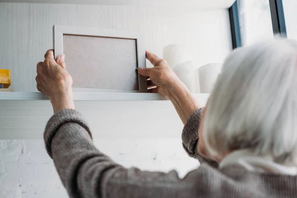 Teilansicht einer Seniorin, die zu Hause leere Fotorahmen aus dem Bücherregal holt — Stockfoto