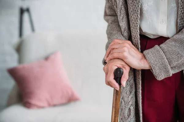 Cropped shot of senior lady with wooden walking stick at home — Stock Photo