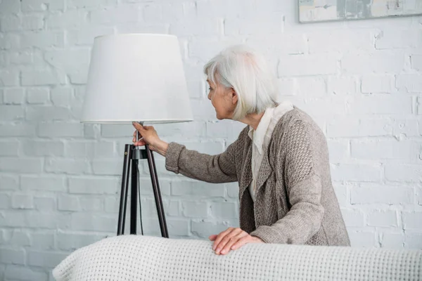 Grey hair lady turning on standing lamp at home — Stock Photo