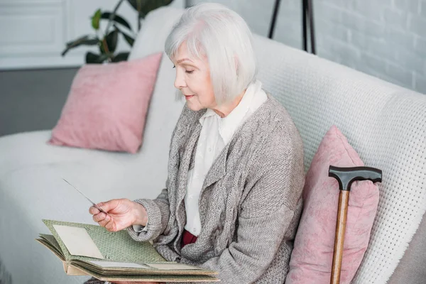 Side view of senior lady with photo album resting on couch at home — Stock Photo