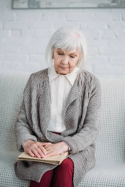 Porträt einer nachdenklichen Seniorin mit Fotoalbum auf Couch zu Hause — Stockfoto