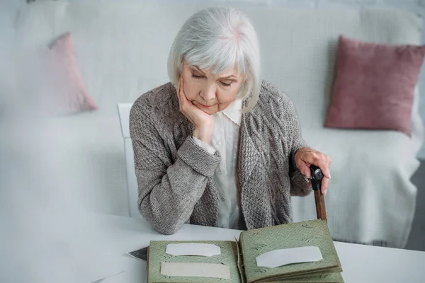 Portrait of grey hair woman looking at photos in photo album at table at home — Stock Photo