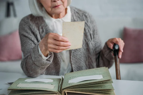 Vista parcial de la mujer mayor mirando la foto del álbum de fotos en la mesa en casa - foto de stock