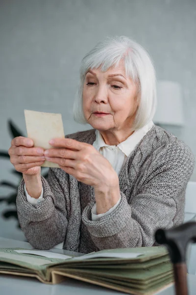 Portrait of grey hair woman looking at photo from photo album at table at home — Stock Photo