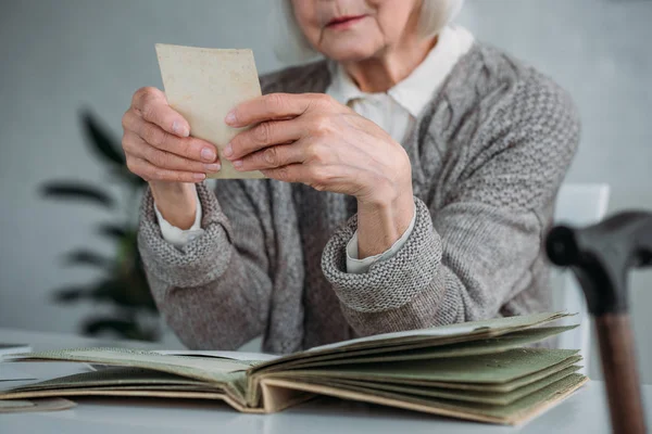 Partial view of senior woman looking at photo from photo album at table at home — Stock Photo