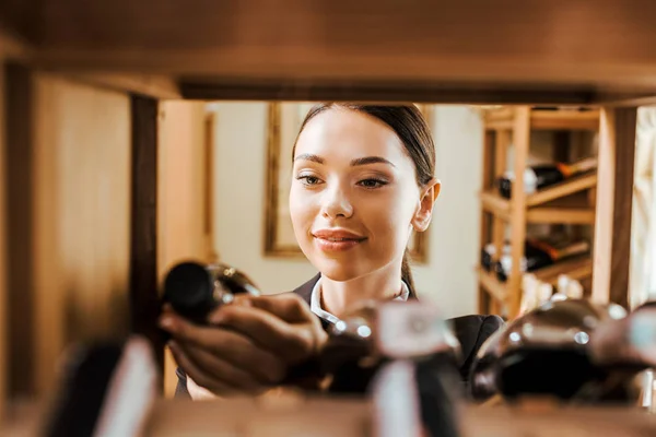 View from shelf at beautiful female wine steward holding bottle at wine store — Stock Photo