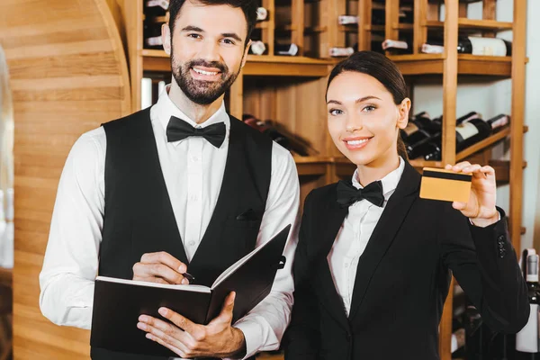 Couple de stewards du vin avec ordinateur portable et carte de crédit dorée regardant la caméra au magasin de vin — Photo de stock