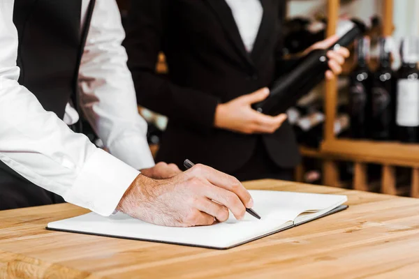 Plan recadré de deux intendants du vin faisant le point sur le vin en magasin — Photo de stock